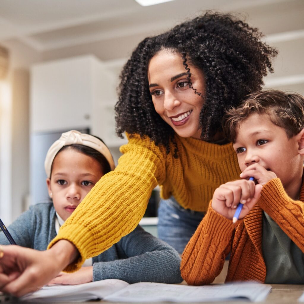 An adult mentor working alongside two young students at a table