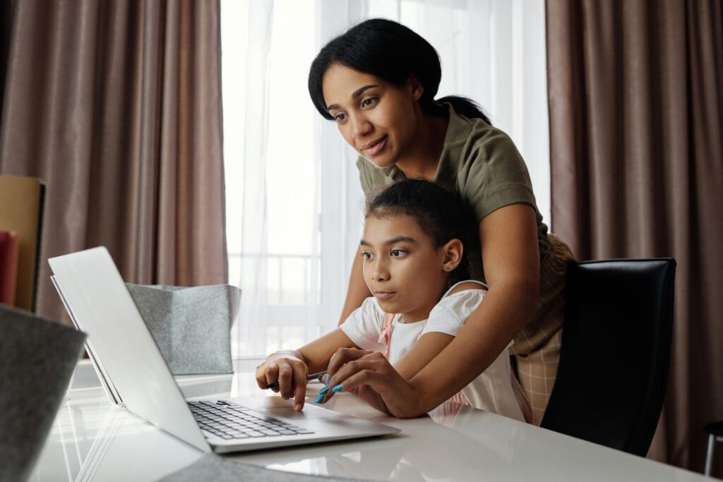 A parent sitting with her daughter and looking over her shoulder at a lesson on the laptop